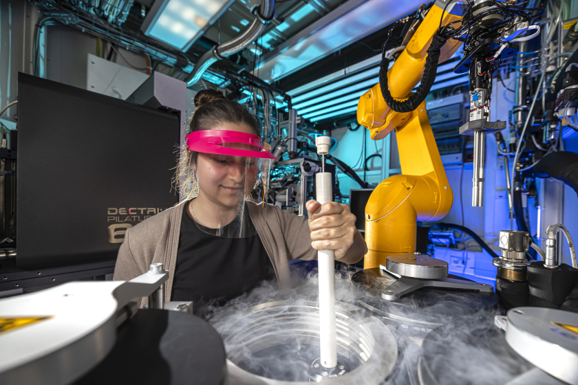 Scientist Tajana Bartels fills the sample container. The yellow robotic arm in the background changes the samples during the measurement.