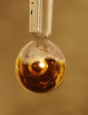 After about 5 seconds, a thin film of metallic water has formed around the NaK drop, recognisable by the golden shimmer.