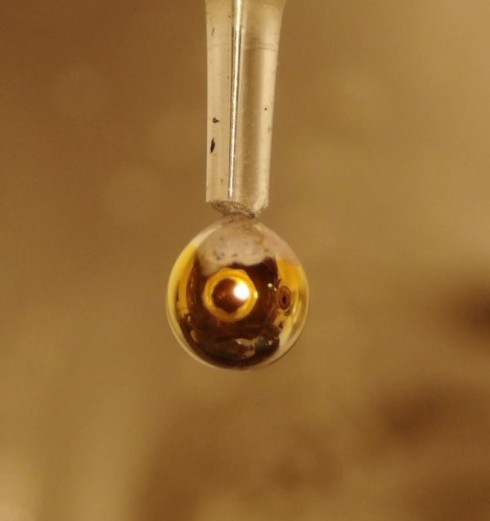 <p>After about 5 seconds, a thin film of metallic water has formed around the NaK drop, recognisable by the golden shimmer.</p>